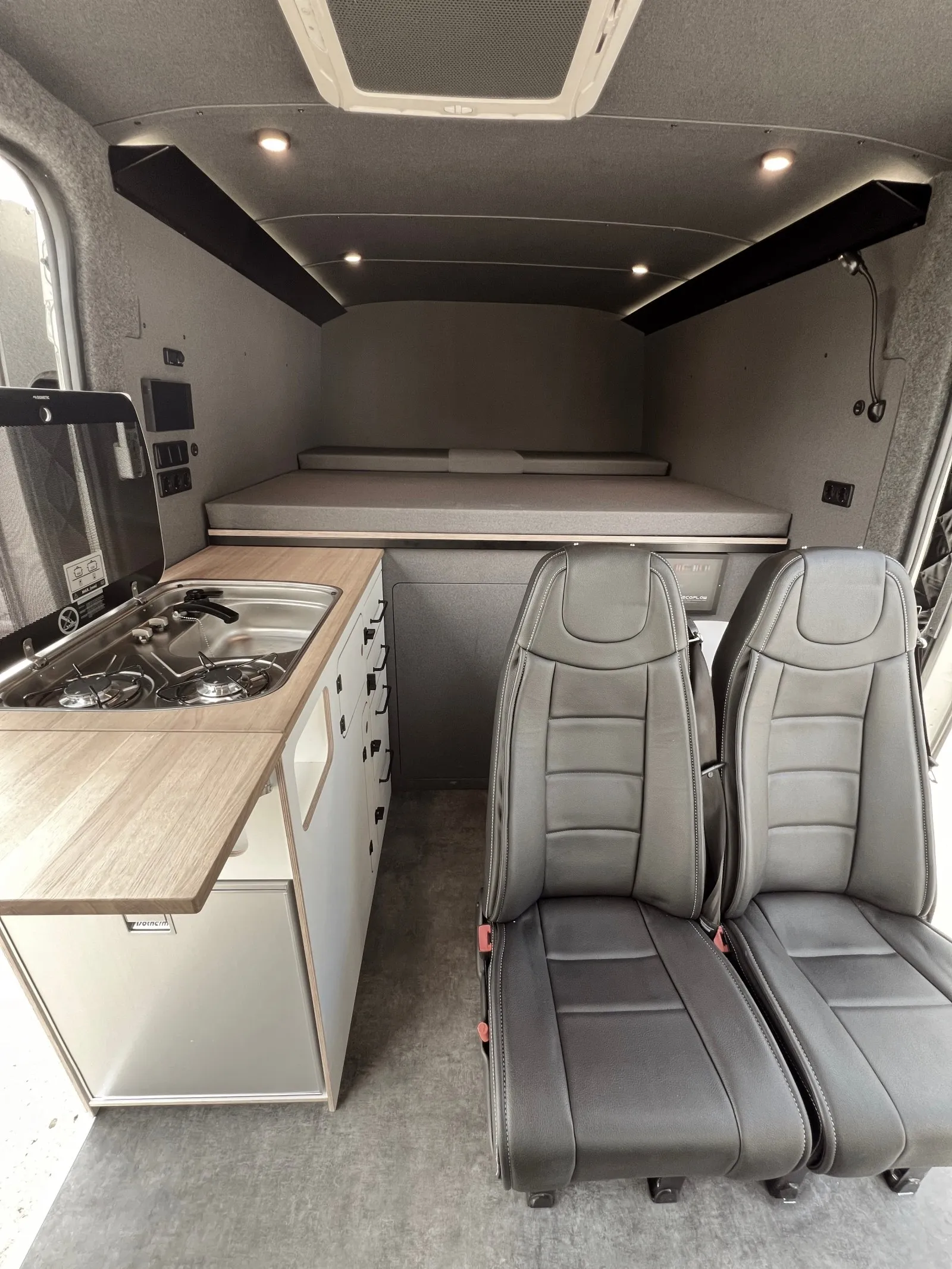 Interior of a converted campervan with kitchen unit, two seats and bed