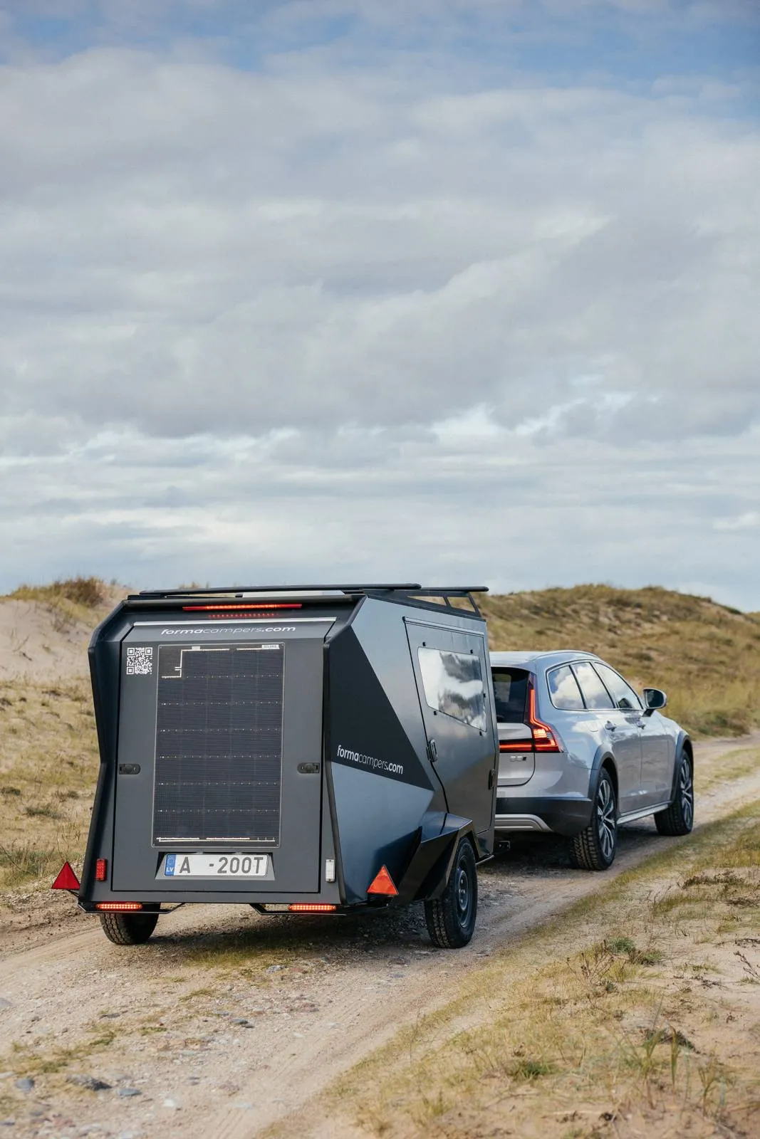 Rear view of a Forma Campers trailer with a solar panel, parked in sand dunes