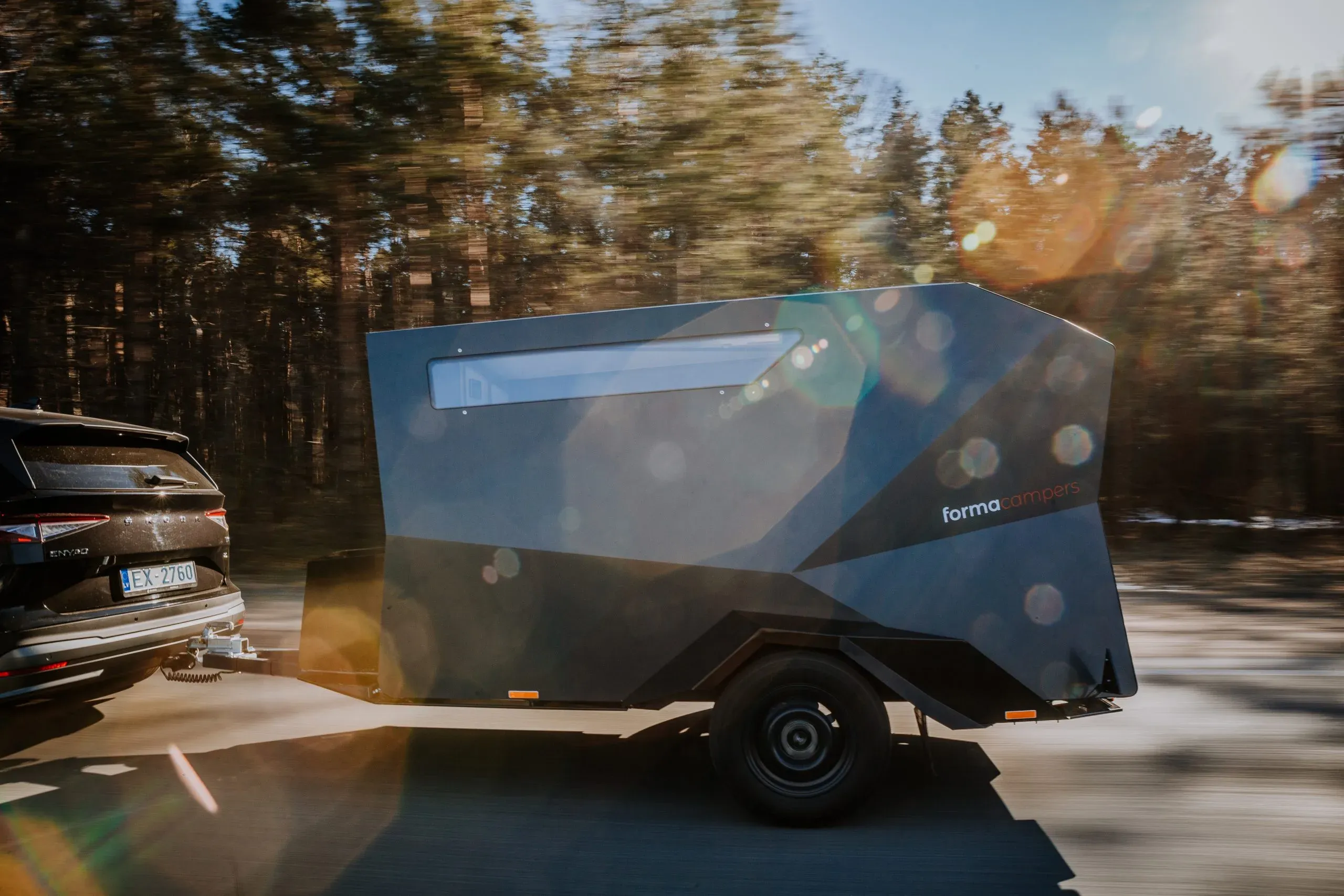 A dark grey Forma Campers trailer being towed along a forest road at speed